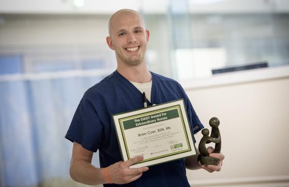 Brian Coer, BSN, RN, clinical nurse holding The Daisy Award certificate and statue.