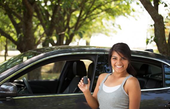 Female teen standing next to car with holding car keys.