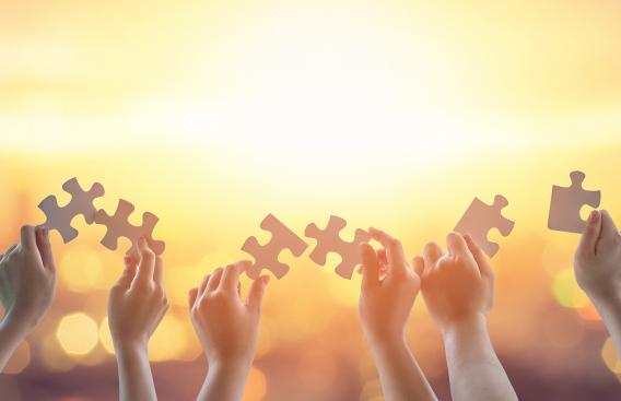 hands holding puzzle pieces against a yellow sky