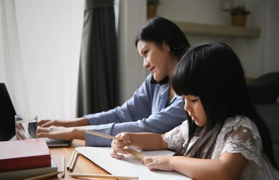 Mother working at computer with daughter drawing
